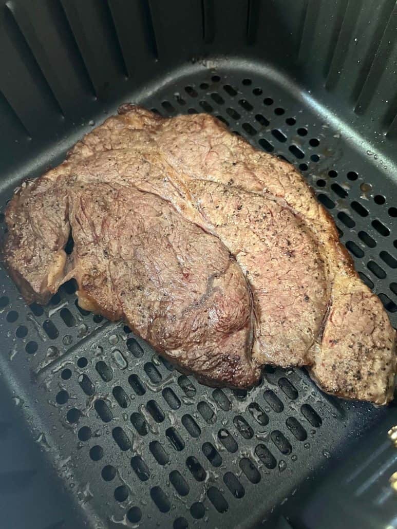 Close-up of boneless chuck steak in an air fryer basket, displaying a perfectly seared, golden-brown crust.