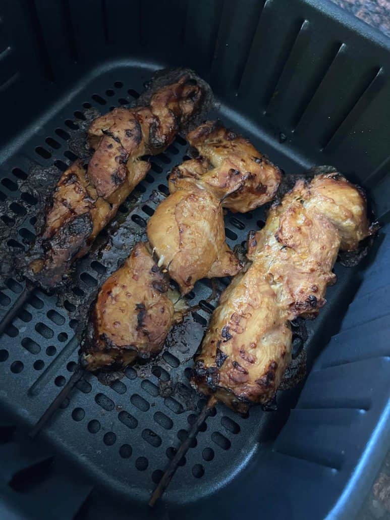 Three air fryer chicken skewers inside on air fryer basket. 