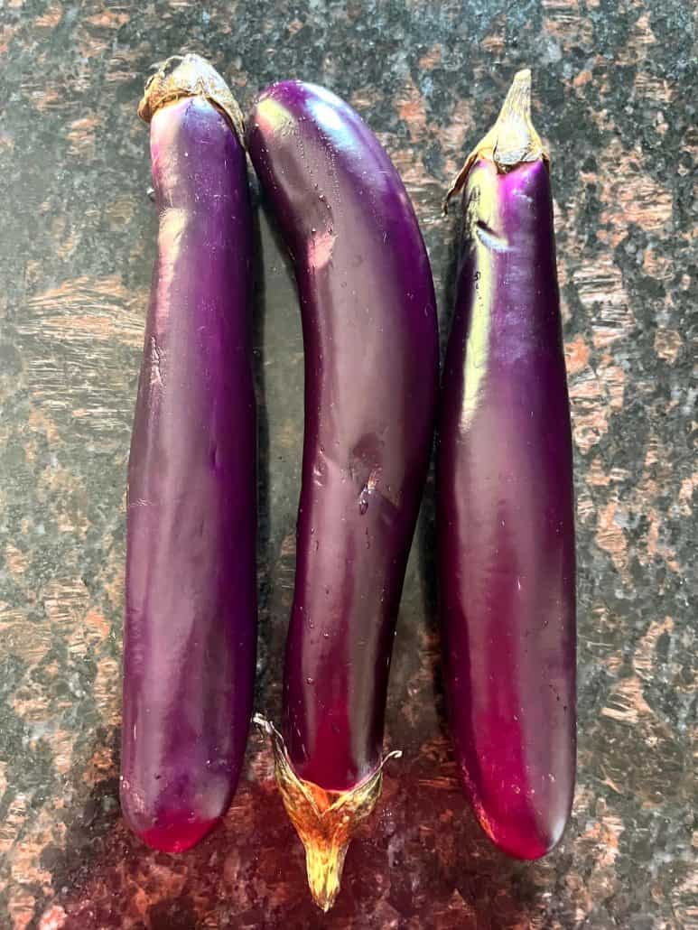 Three fresh Chinese eggplants laid side by side on a kitchen countertop, ready for preparation in a delicious air fryer recipe.