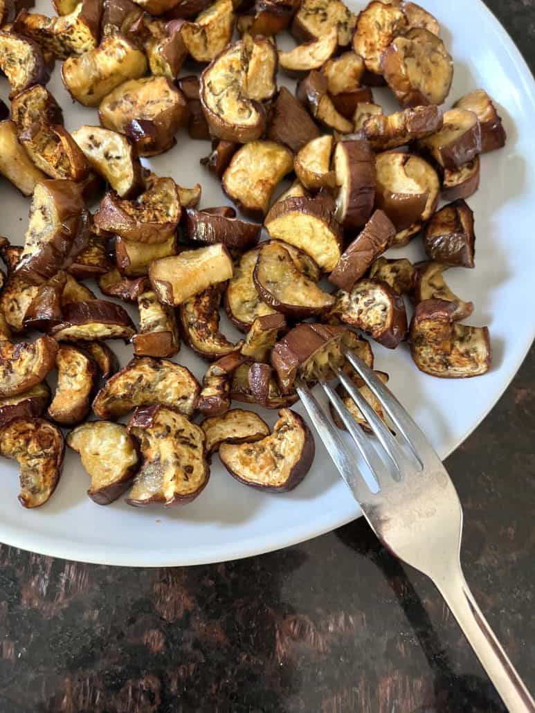 A plate of roasted Chinese eggplant pieces with a fork resting on the side.