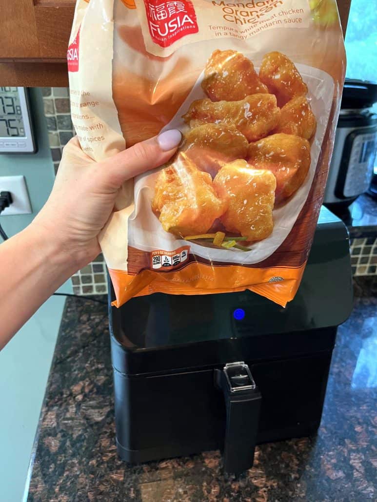 A package of Fusia Mandarin Orange Chicken from Aldi over an air fryer, showing the start of the air fryer cooking process for a quick and crispy meal