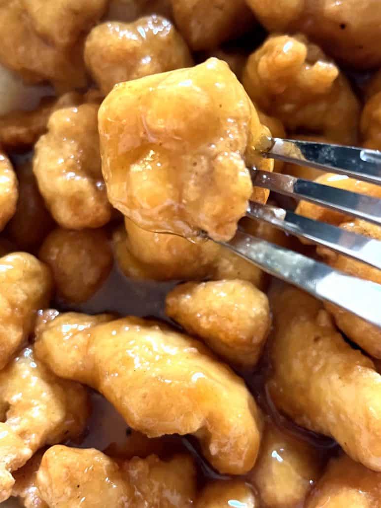 Close-up of a fork holding a piece of crispy air-fried Fusia Mandarin Orange Chicken, highlighting it's golden texture and glossy orange sauce