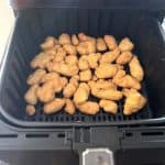 Crispy frozen orange chicken pieces cooking in an air fryer basket, demonstrating how Aldi's Fusia Mandarin Orange Chicken cooks perfectly in the air fryer