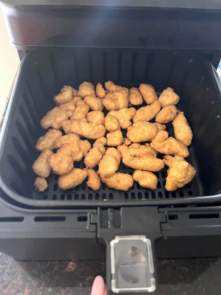 Crispy frozen orange chicken pieces cooking in an air fryer basket, demonstrating how Aldi's Fusia Mandarin Orange Chicken cooks perfectly in the air fryer