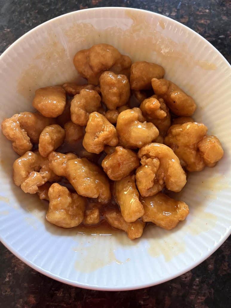 A close-up of a bowl filled with crispy air-fried Fusia Mandarin Orange Chicken, coated in a sweet and tangy orange sauce.