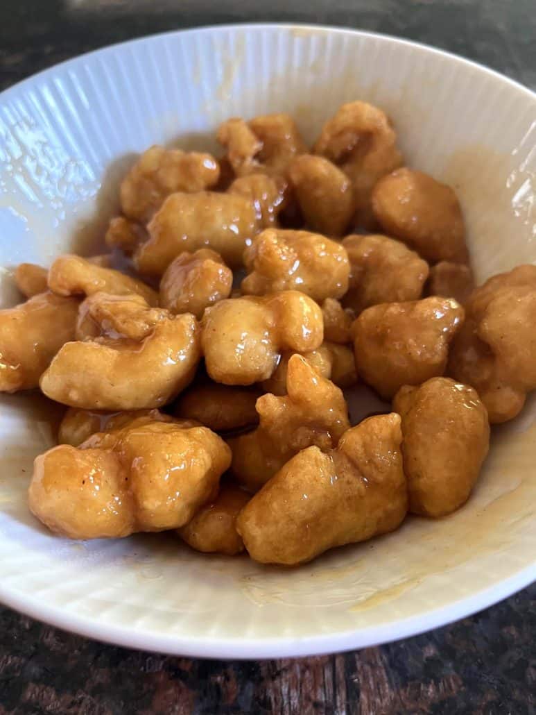 A side view of a bowl filled with crispy air-fried Fusia Mandarin Orange Chicken, showcasing the golden-brown coating covered in a sweet orange sauce.