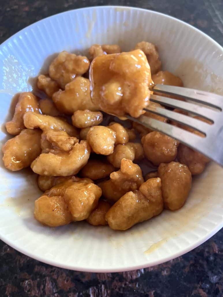 A fork picking up the crispy texture Mandarin Orange Chicken, highlighting the sweet orange glaze