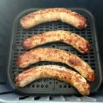 Four pieces of Greek sausage inside an air fryer basket.