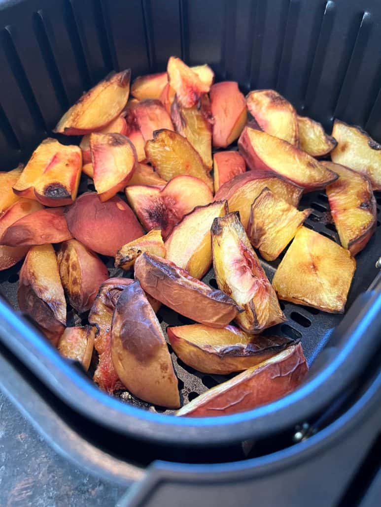 A batch of perfectly caramelized peach slices in an air fryer basket, showing the golden-brown edges.