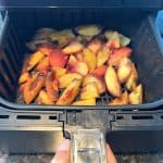 Opening the air fryer basket, revealing the perfectly roasted peach slices.