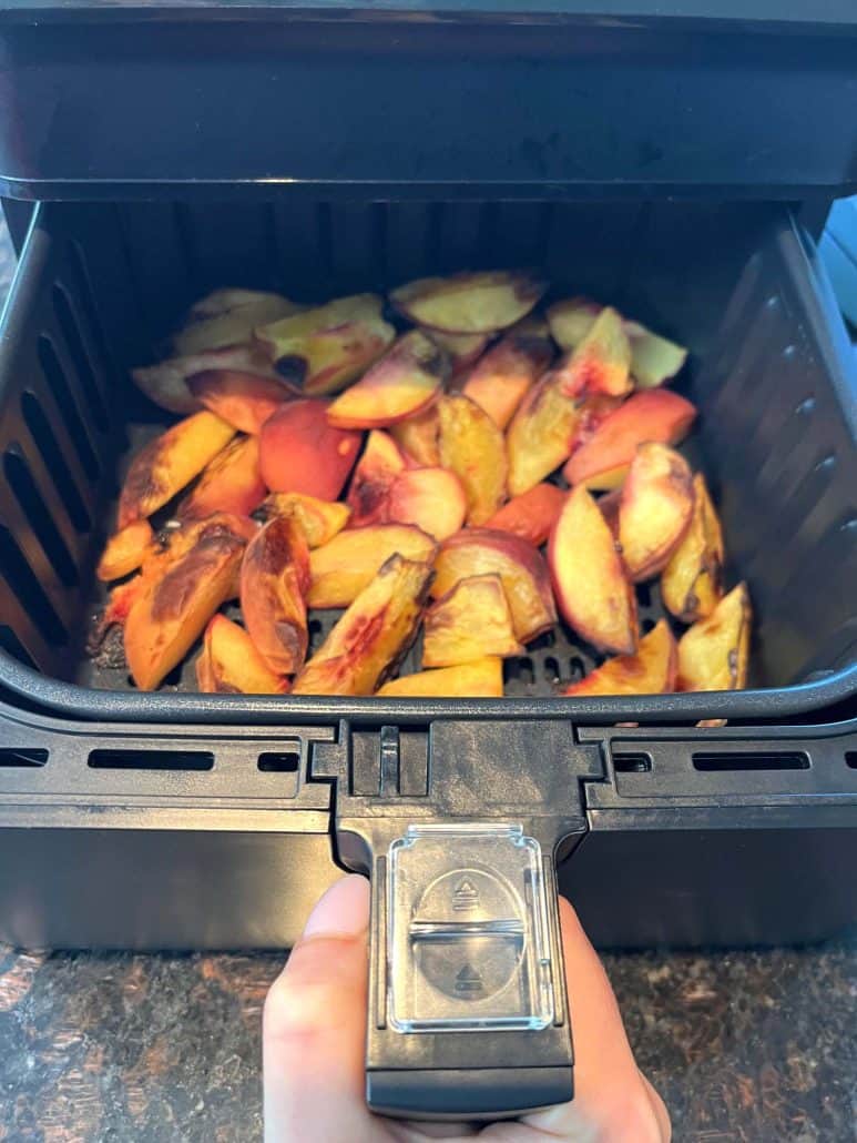 Opening the air fryer basket, revealing the perfectly roasted peach slices. 