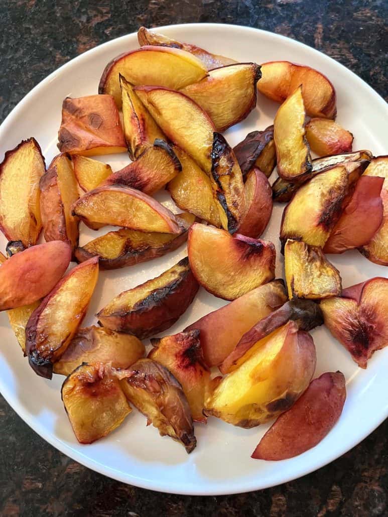 A plate of roasted peach slices fresh from the air fryer, showcasing their caramelized edges and soft texture.