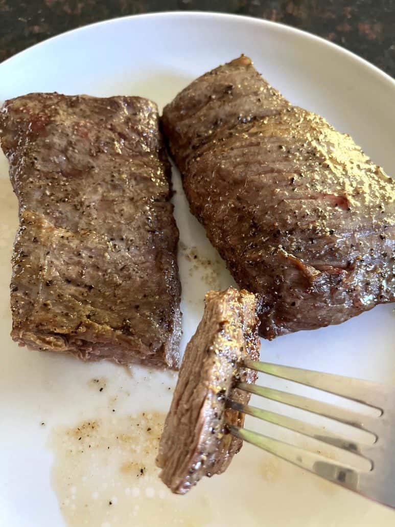 Two cooked skirt steaks on a white plate with a slice cut, showing the tender, juicy inside and crispy exterior.