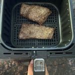 Two seasoned skirt steaks cooking in an air fryer basket, illustrating the air frying process for the air fryer skirt steak recipe.