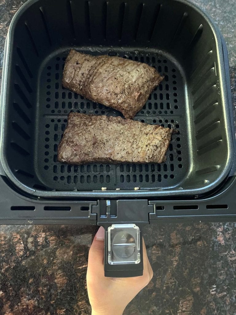 Two seasoned skirt steaks cooking in an air fryer basket, illustrating the air frying process for the air fryer skirt steak recipe.