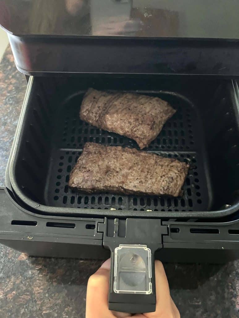 Two juicy skirt steaks cooking in an air fryer basket.