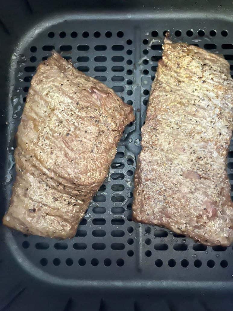 Close-up of two cooked skirt steaks in an air fryer basket, showing the perfectly browned exterior as part of the air fryer skirt steak recipe.