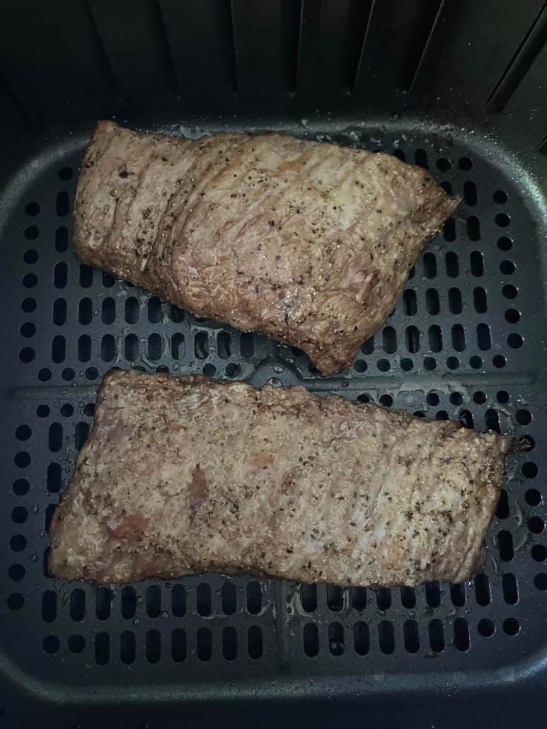 Two browned skirt steaks in an air fryer basket after cooking, highlighting the crispy, seasoned exterior from the air fryer skirt steak recipe.