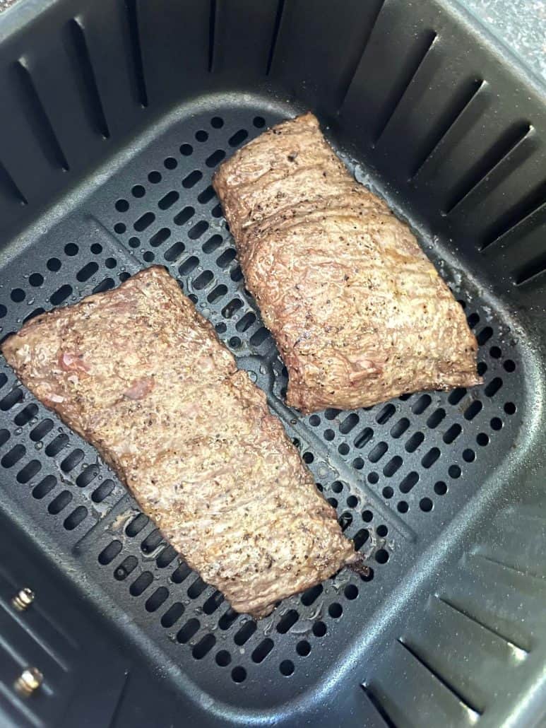 Two fully cooked skirt steaks in an air fryer basket with a crispy, golden-brown exterior, ready to be served as part of the air fryer skirt steak recipe.