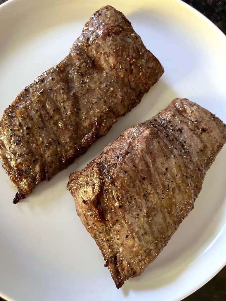 Two cooked skirt steaks resting on a white plate, showcasing their perfectly browned exterior after air frying.