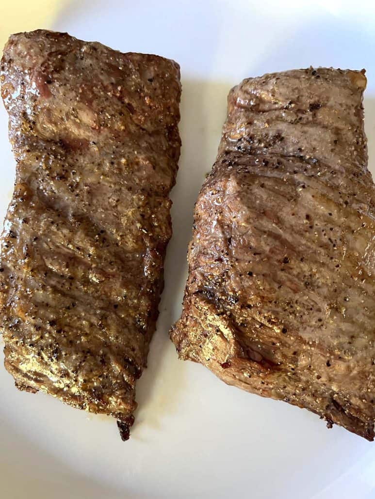 Close-up of two cooked skirt steaks resting on a white plate, highlighting their golden-brown, crispy exterior from air frying.