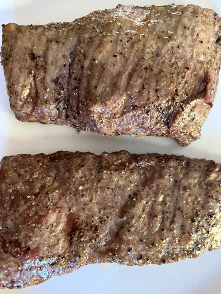 Close-up of two air-fried skirt steaks on a white plate, showing the well-seasoned and crispy exterior after cooking.