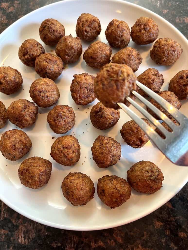 A fork holding a freshly cooked vegan meatball above a plate full of golden-brown meatballs.