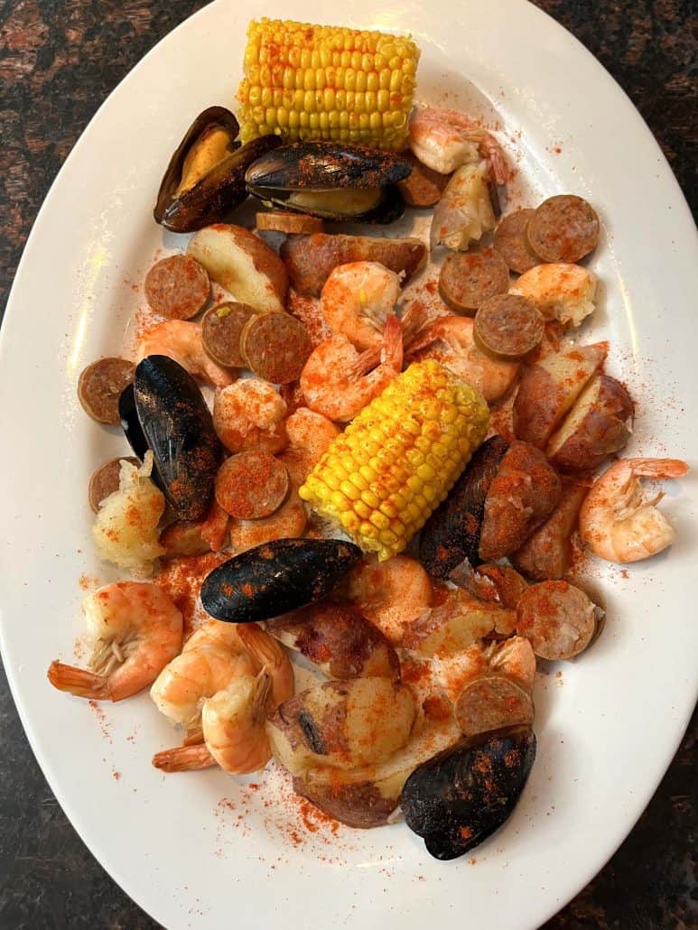 A vibrant seafood boil featuring shrimp, mussels, corn on the cob, sausage slices, red potatoes, and Cajun seasoning.