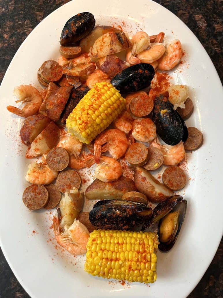 An appealing serving platter filled with cooked shrimp, mussels, sausage, red potatoes, and corn on the cob from Aldi's Frozen Seafood Boil, all seasoned with Cajun spices and ready to serve.