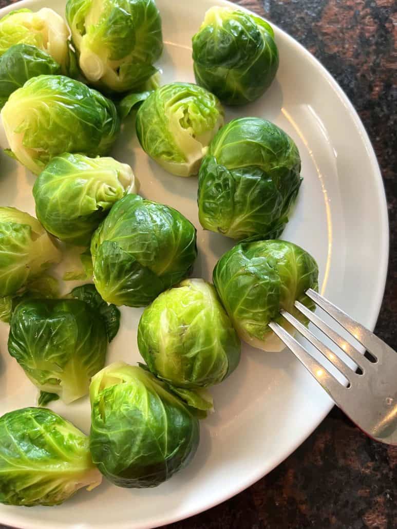 A fork pressing into a Brussels sprout, showcasing their tender texture.