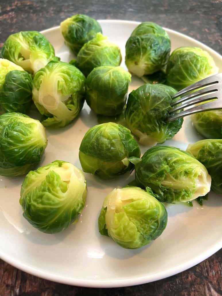 A fork piercing a tender Brussels sprout on a plate.