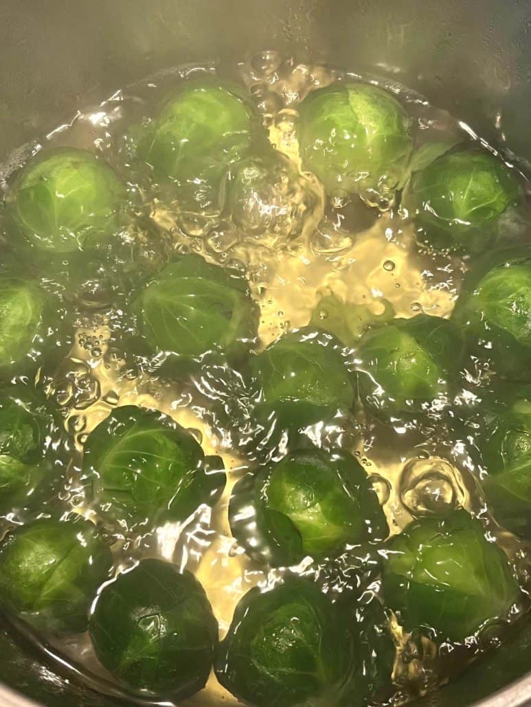 Close-up of Brussels sprouts boiling in a pot of water, showing the vibrant green color.