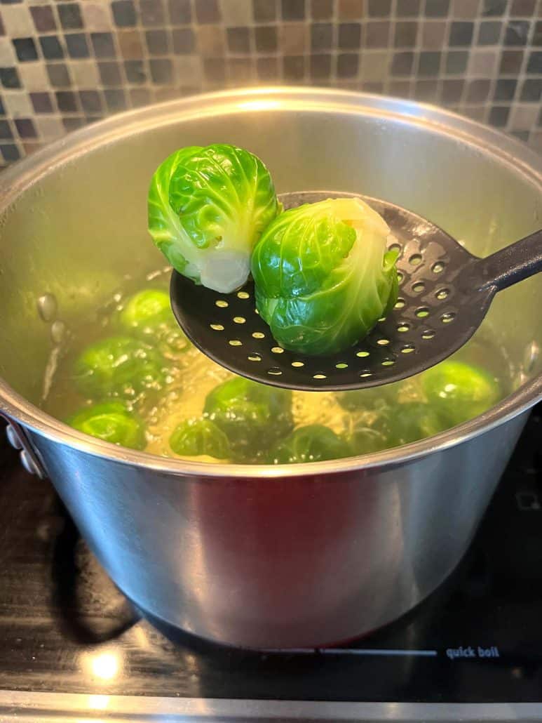 Two bright green boiled Brussels sprouts being lifted from a pot with a slotted spoon.