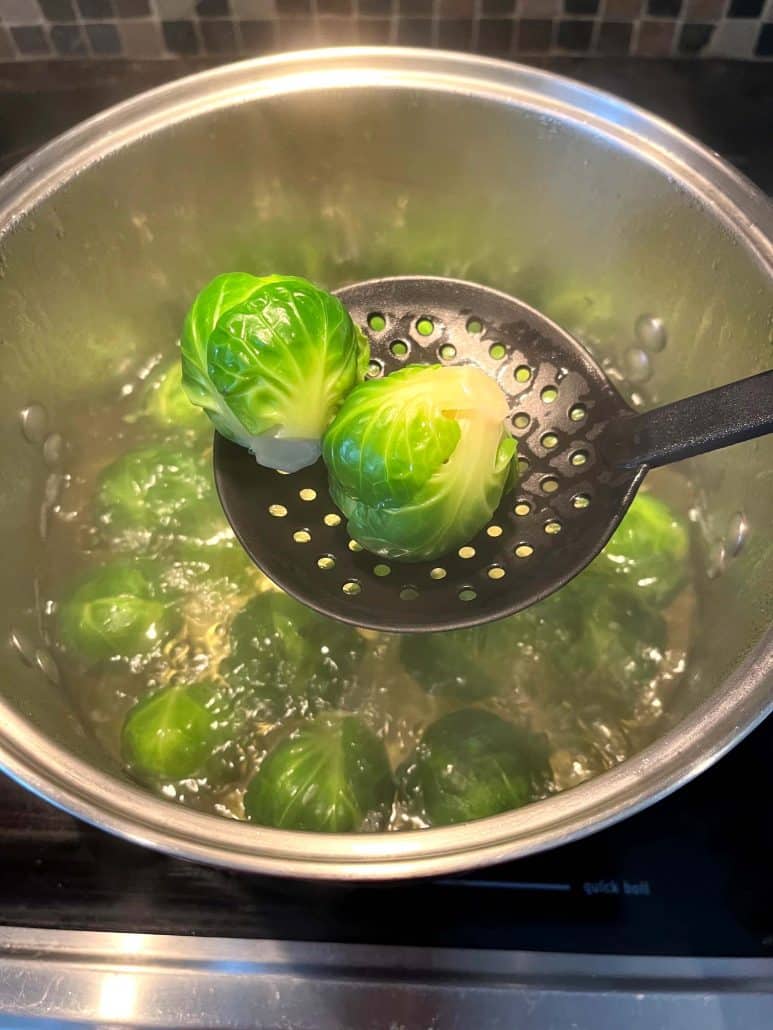 Two boiled Brussels sprouts being lifted from a pot of boiling water with a slotted spoon.