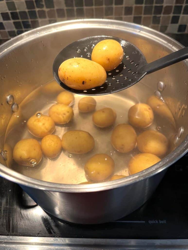 Checking if the small boiled potatoes are tender by lifting them with a slotted spoon during the cooking process.