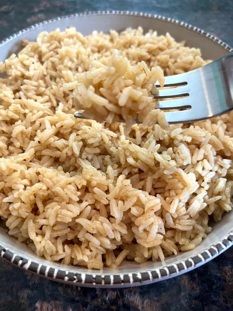 A fork lifting a portion of fluffy bone broth rice from a bowl, highlighting the light and well-separated grains.