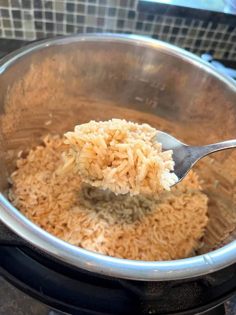 A fork lifting a portion of perfectly cooked bone broth rice from an Instant Pot, highlighting the fluffy texture achieved through pressure cooking.