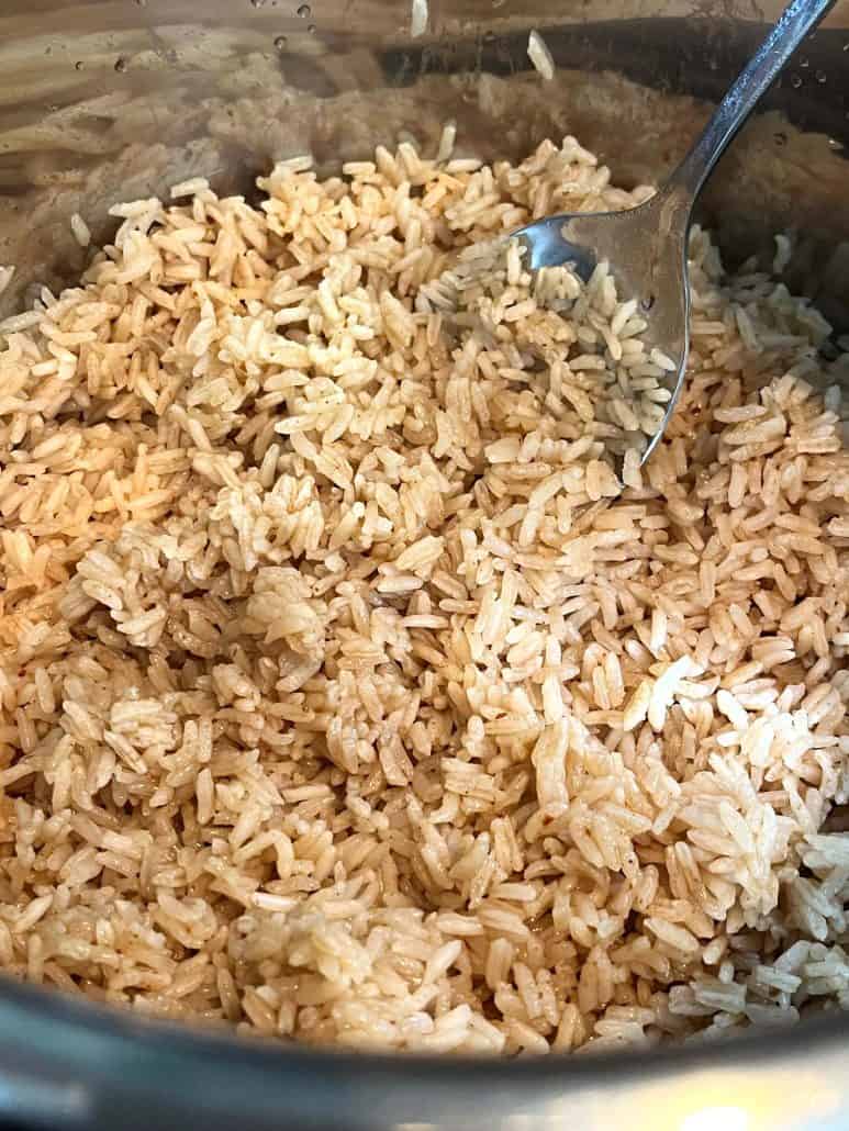 A close-up view of fluffy bone broth rice in an Instant Pot with a fork resting in the pot, showing the perfectly separated grains after cooking.