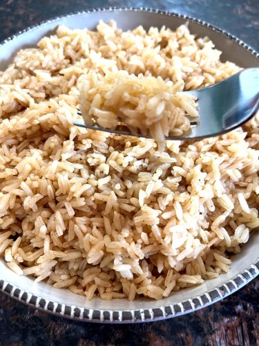 A bowl of perfectly cooked fluffy rice, showing a fork lifting a portion to highlight the light and separate grains.