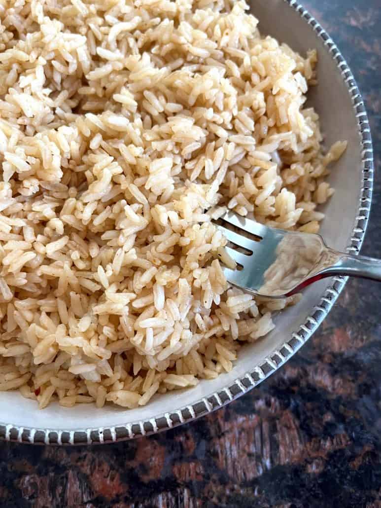 A close-up of a bowl of bone broth rice with a fork resting in the rice, highlighting the fluffy texture and individual grains.