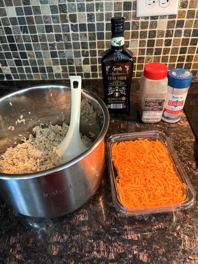 Ingredients for Carrot Rice, including cooked rice, shredded carrots, olive oil, salt, and pepper, displayed on a kitchen countertop, ready for preparation.