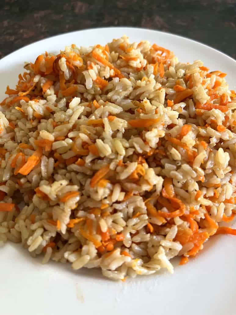 A close-up of Carrot Rice on a white plate, featuring a mix of fluffy rice and vibrant shredded carrots, showcasing its appealing texture and color.