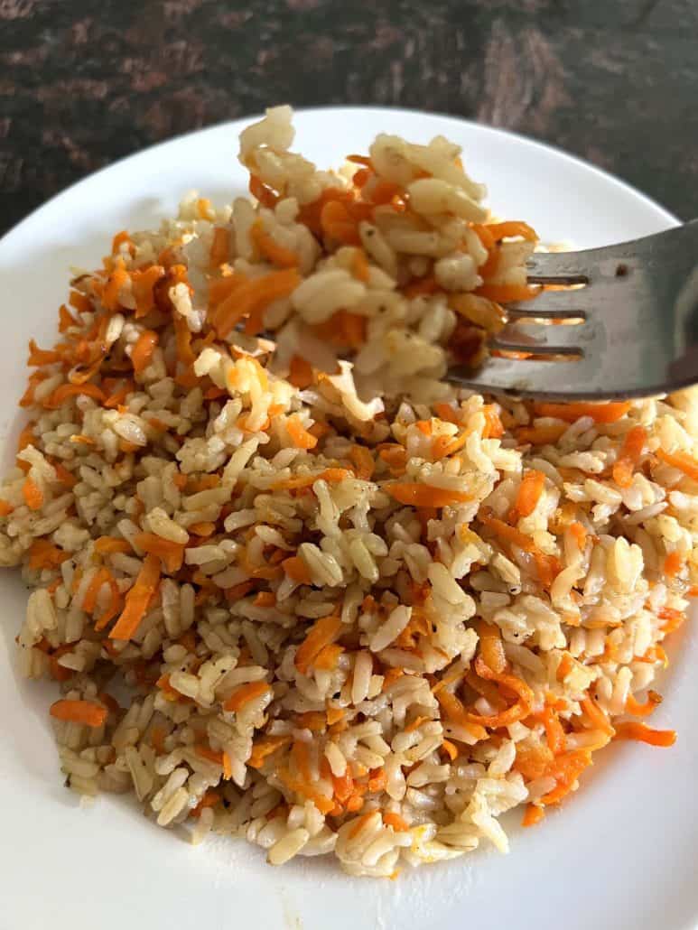 A fork lifting a bite of Carrot Rice from a plate, highlighting the combination of fluffy rice and vibrant shredded carrots, ready to be tasted.