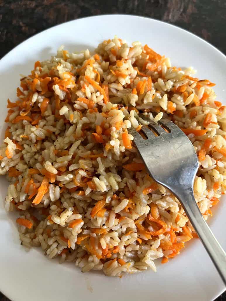 A plate of Carrot Rice with a fork resting on top, ready to be enjoyed as a healthy and flavorful dish.