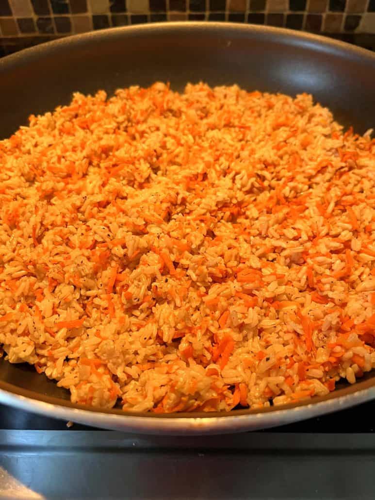 Close-up view of a pan filled with Carrot Rice, highlighting the vibrant mix of cooked rice and shredded carrots, freshly prepared and ready to enjoy.