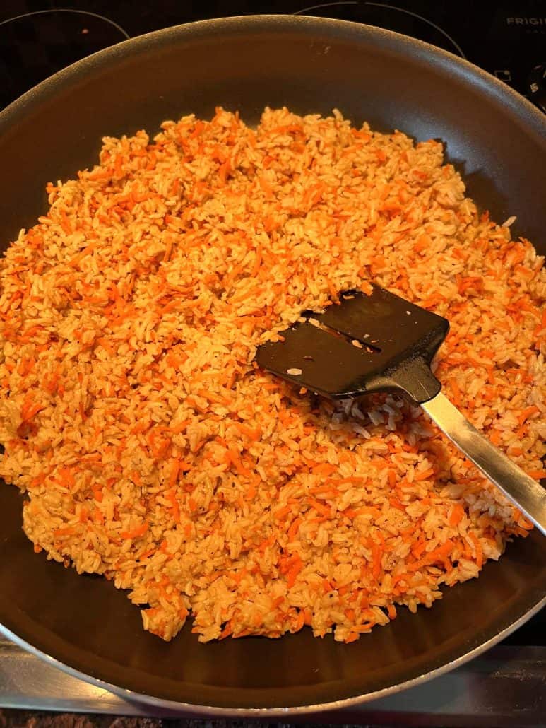 A pan filled with Carrot Rice, featuring a spatula resting on the rice mixture, ready to be stirred or served.