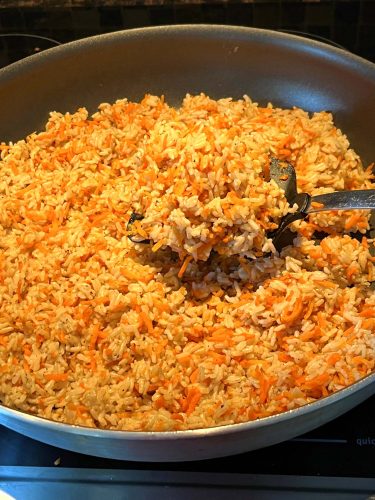 A close-up of a pan filled with Carrot Rice, showing a spatula lifting a portion of the cooked mixture of rice and shredded carrots.