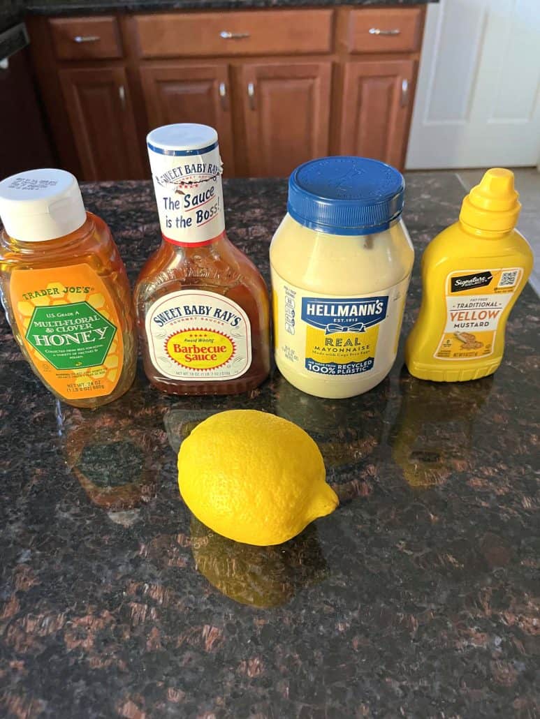 The key ingredients for homemade Chick-Fil-A sauce: honey, barbecue sauce, mayonnaise, mustard, and a lemon, laid out on a kitchen counter.