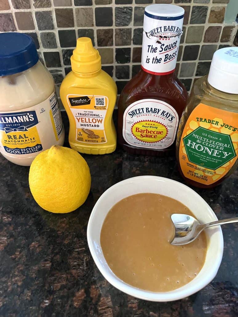 A bowl of homemade Chick-Fil-A sauce next to the key ingredients: mayonnaise, yellow mustard, barbecue sauce, honey, and a lemon.