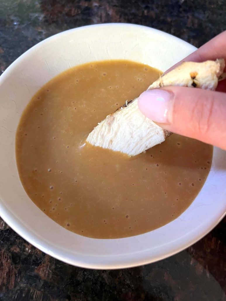 A hand dipping a piece of chicken into a bowl of smooth, homemade Chick-Fil-A sauce, showcasing the creamy texture of this easy copycat recipe.